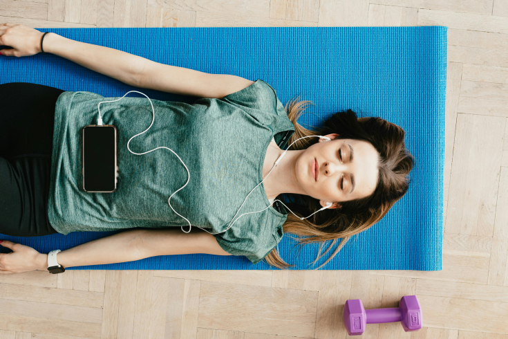 A woman laying on a yoga mat with headphones in