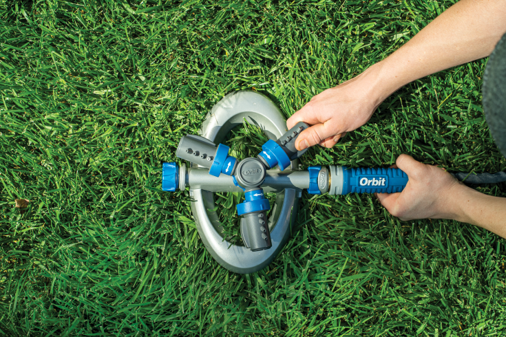Hands turning on an Orbit sprinkler unit in a green lawn