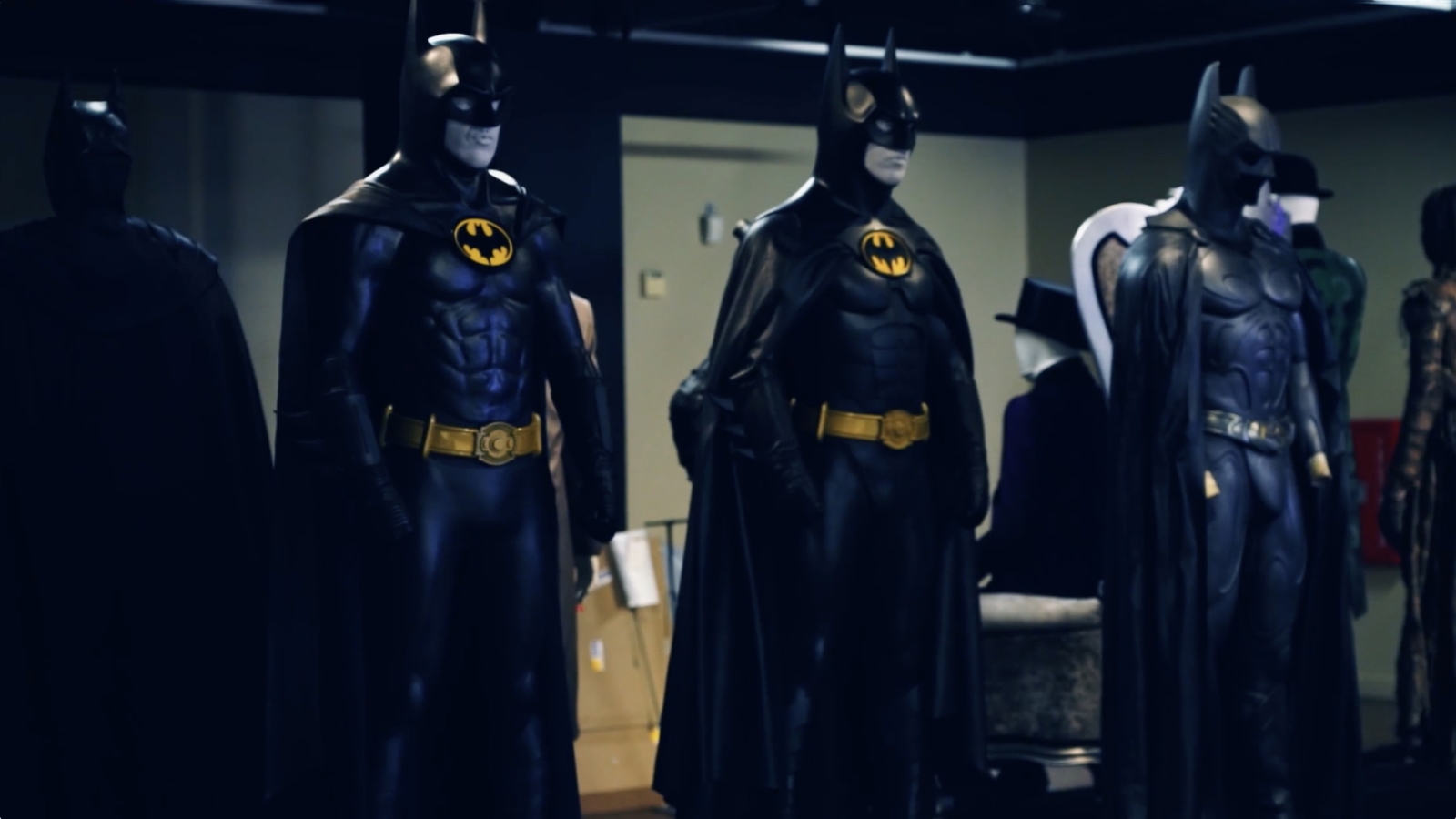 Three Batman costumes on display in the Batman Experience