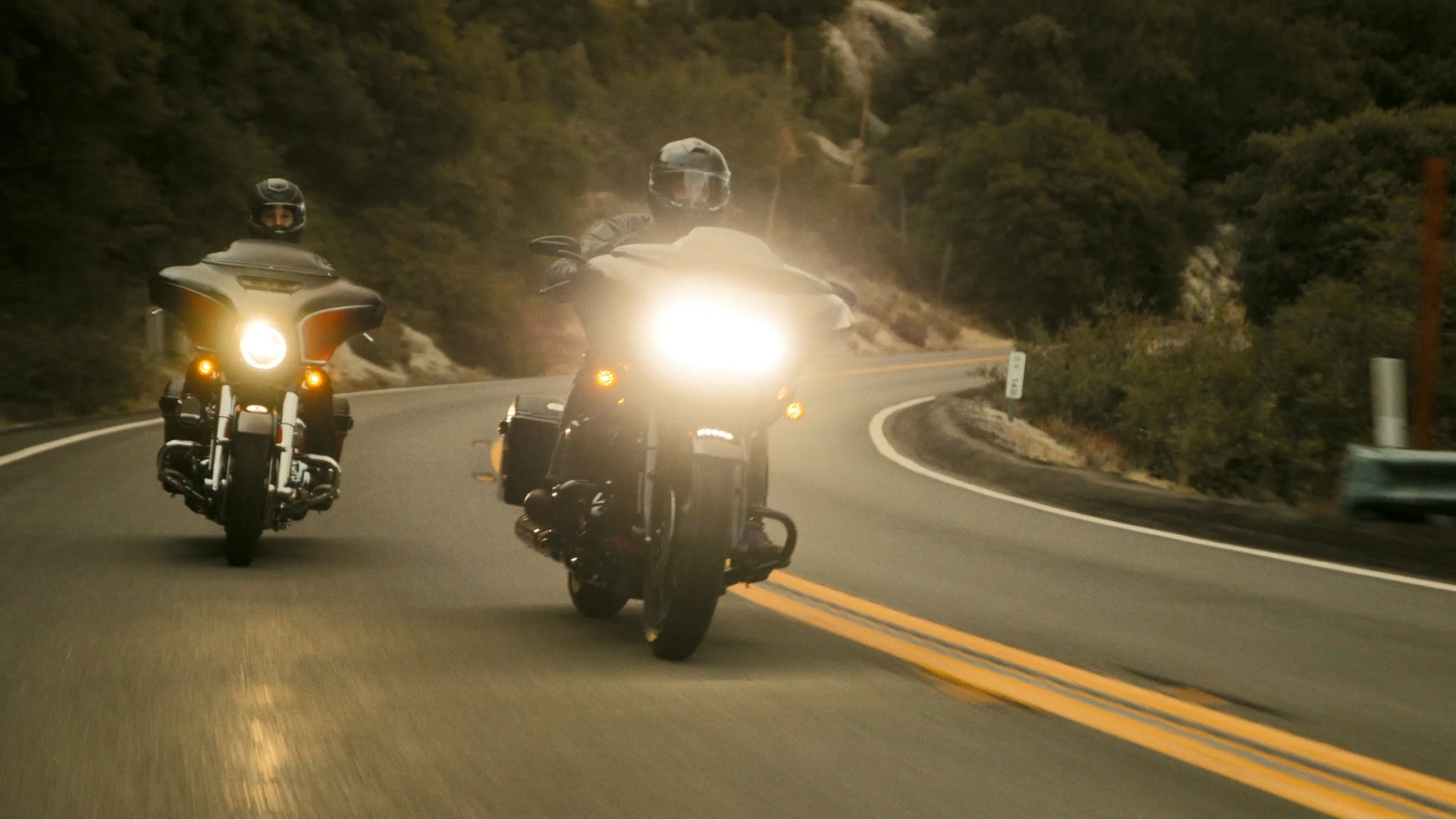 Two people riding Harley Davidson motorcycles down the road