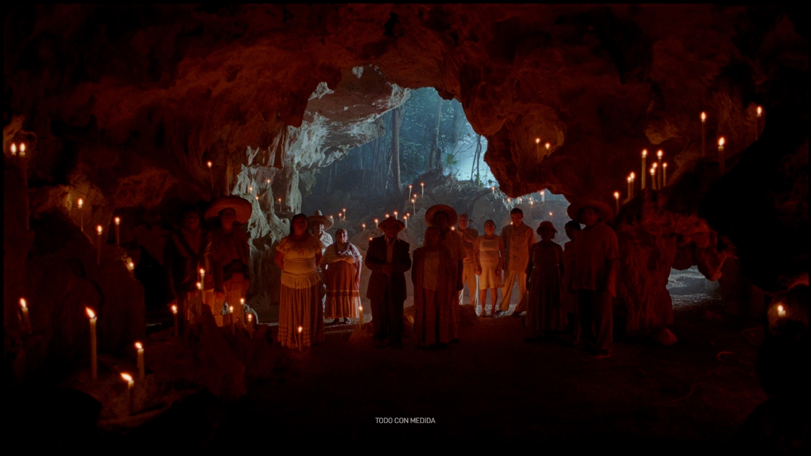 A large group of people hold candles inside a cave