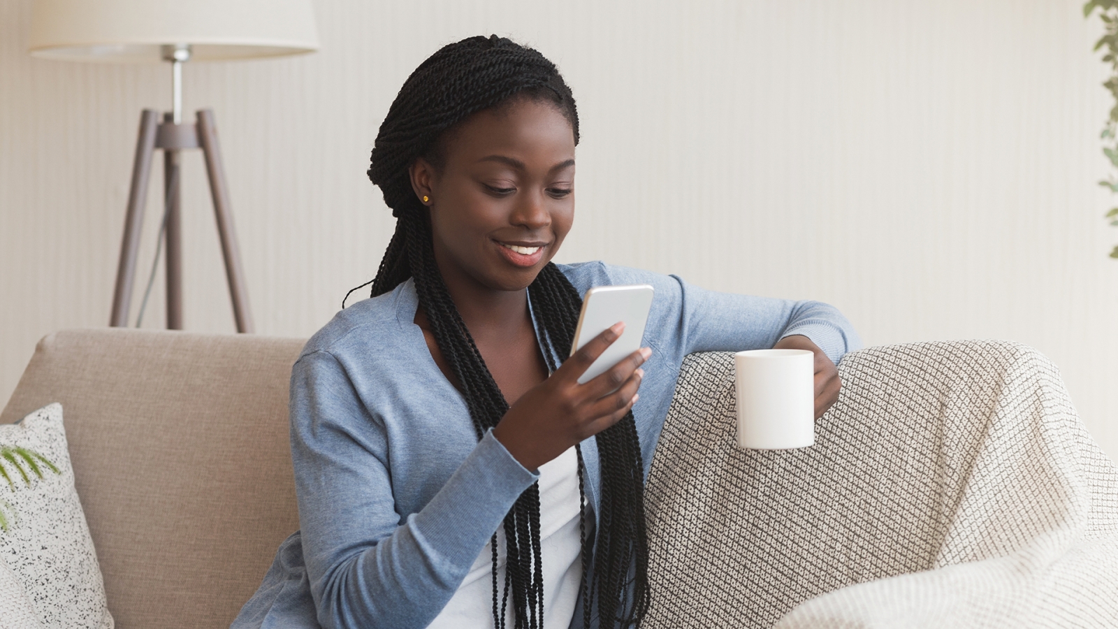 A person looking at their phone and enjoying a cup of coffee on the couch