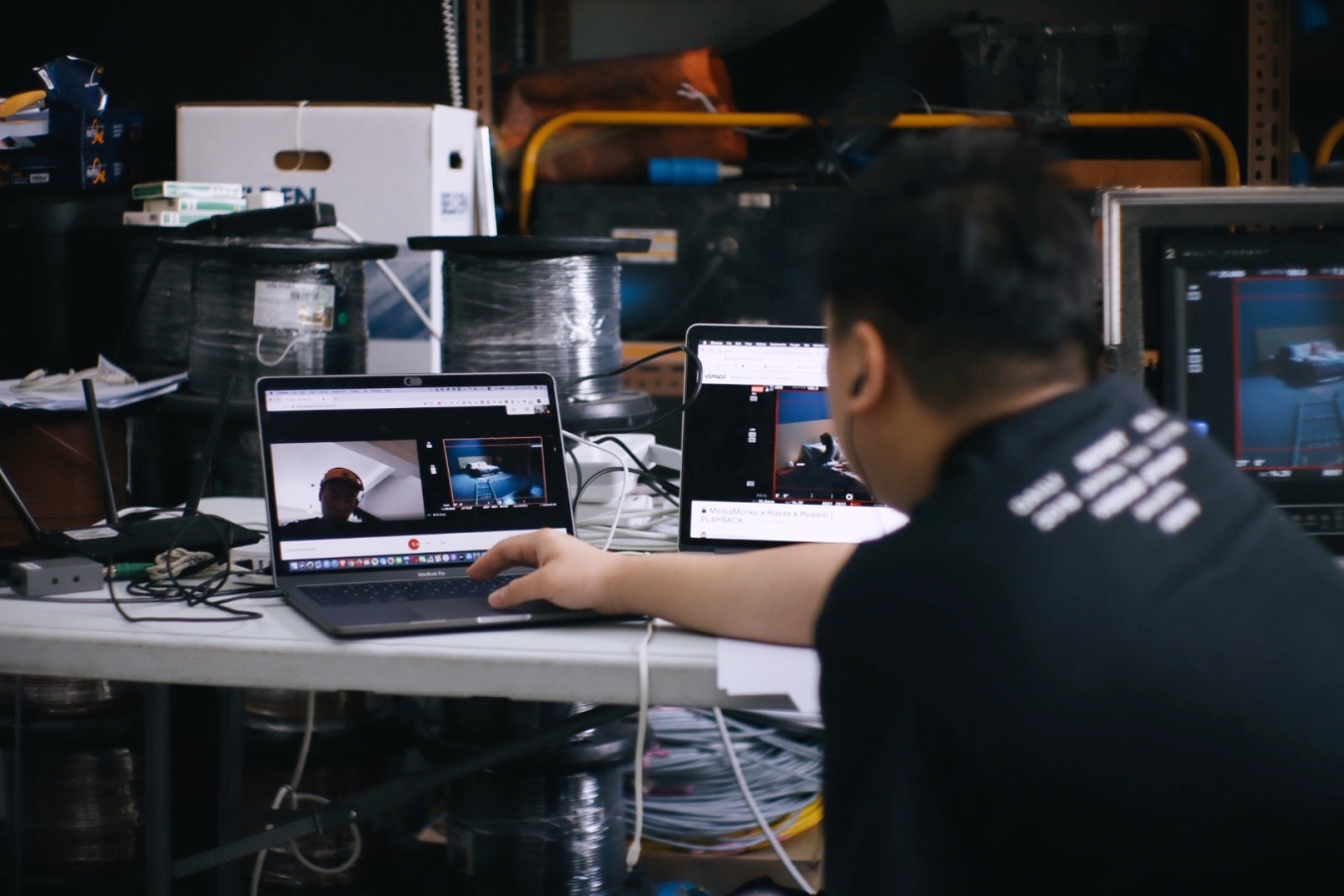 A person working on two laptops doing a remote shoot of a live event