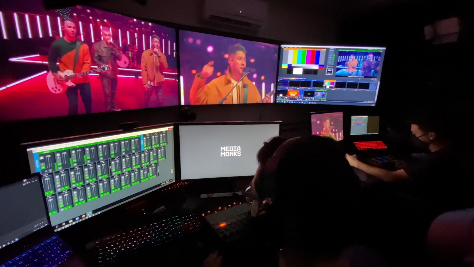 People sitting behind a broadcast booth watching screens with video and audio