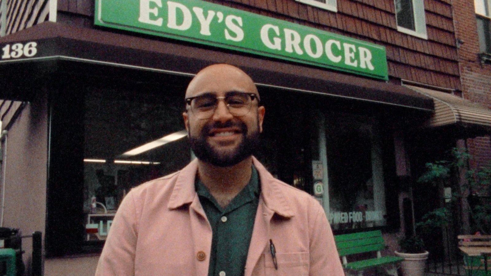 A person stands in front of a grocery store smiling