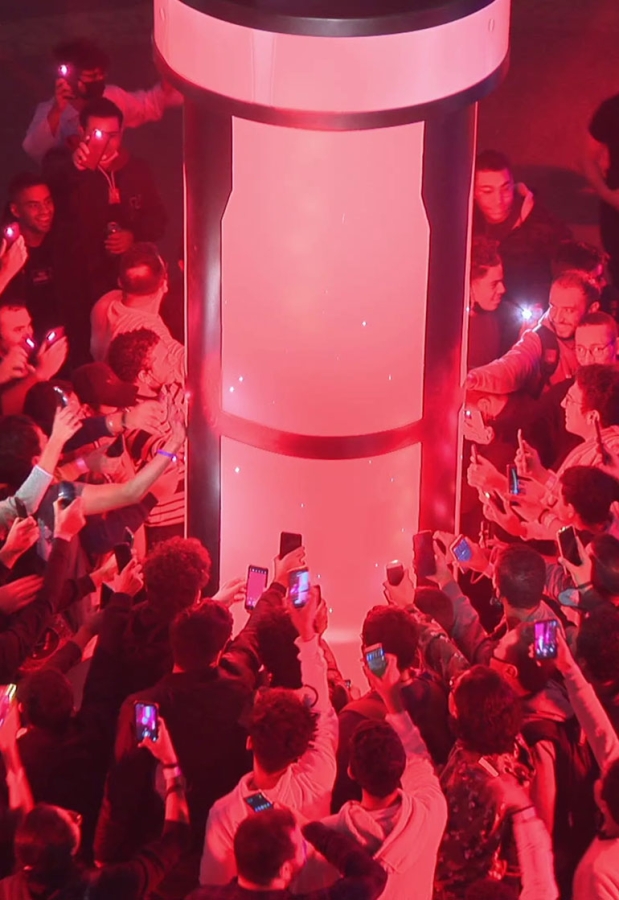 A group of people surrounding an red lit tube taking videos with their phones