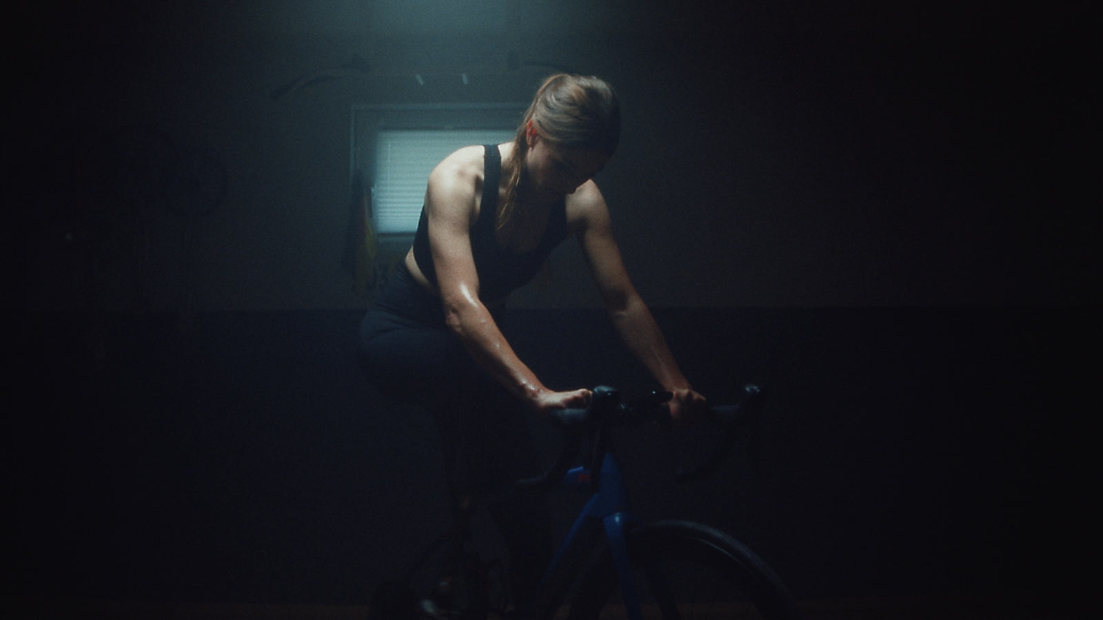 Dark image of a room with in the middle a woman highlighted who is working out on a bike. 