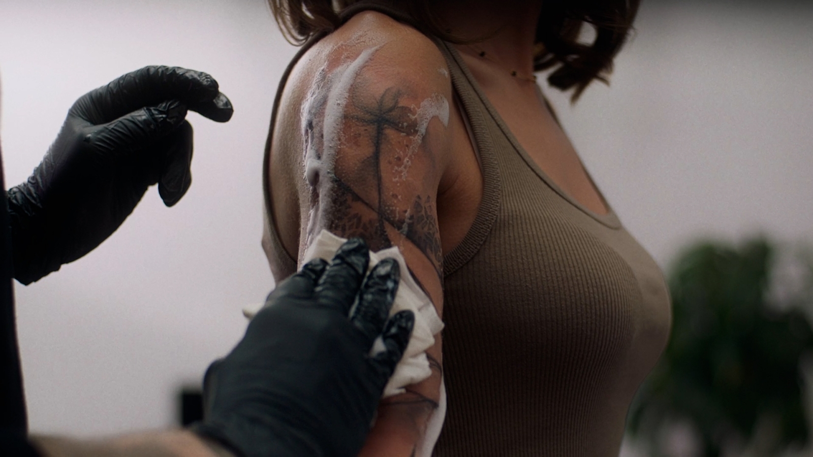 A closeup of the side arm of a women. She just had a tattoo and the tattoo artist is cleaning the fresh tattoo.