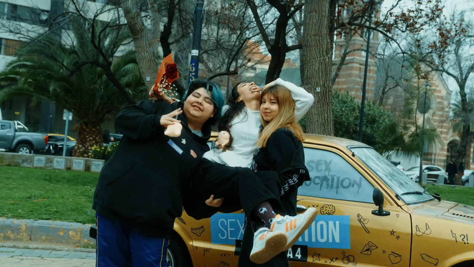 Three bystanders celebrating in front of the yellow taxi sex education car