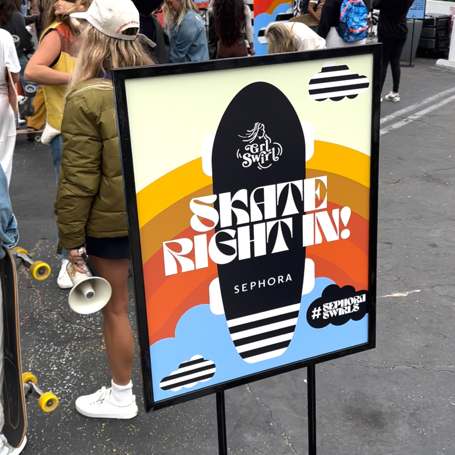 The image features a colorful promotional sign that encourages people to "Skate Right In!" for a Sephora event, with a skateboard graphic and a vibrant rainbow background, surrounded by a crowd of people.