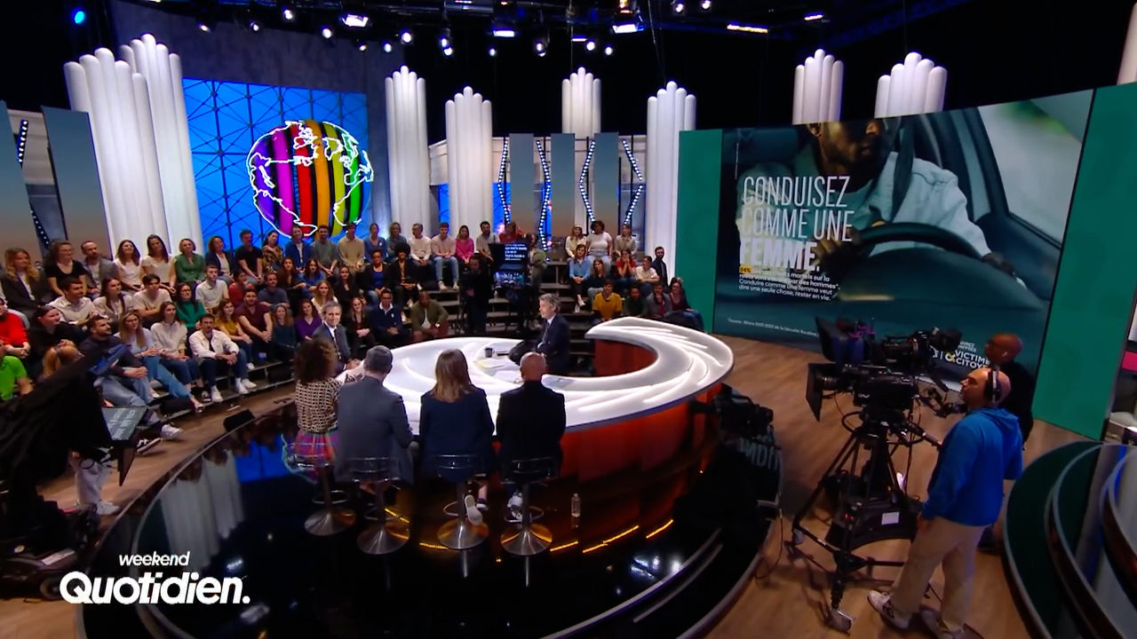 The image shows a lively television studio with a panel discussion taking place in front of an audience, featuring a large display screen that promotes the message "CONDUISEZ COMME UNE FEMME," advocating for safer driving habits.