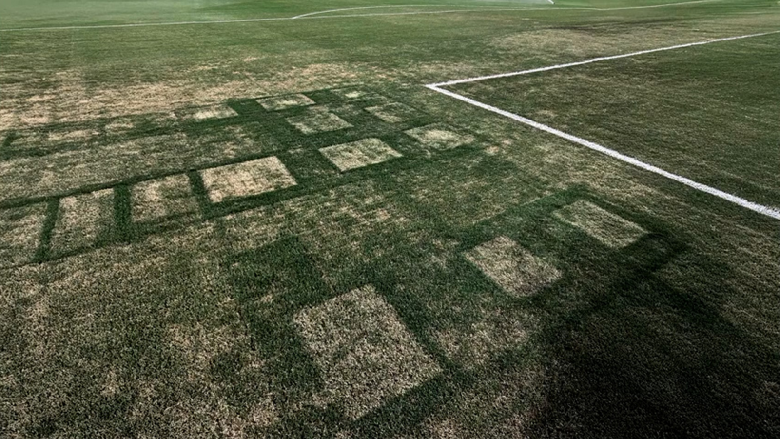 The image shows a football field with a shadow casting a pattern of rectangles and squares on the grass.