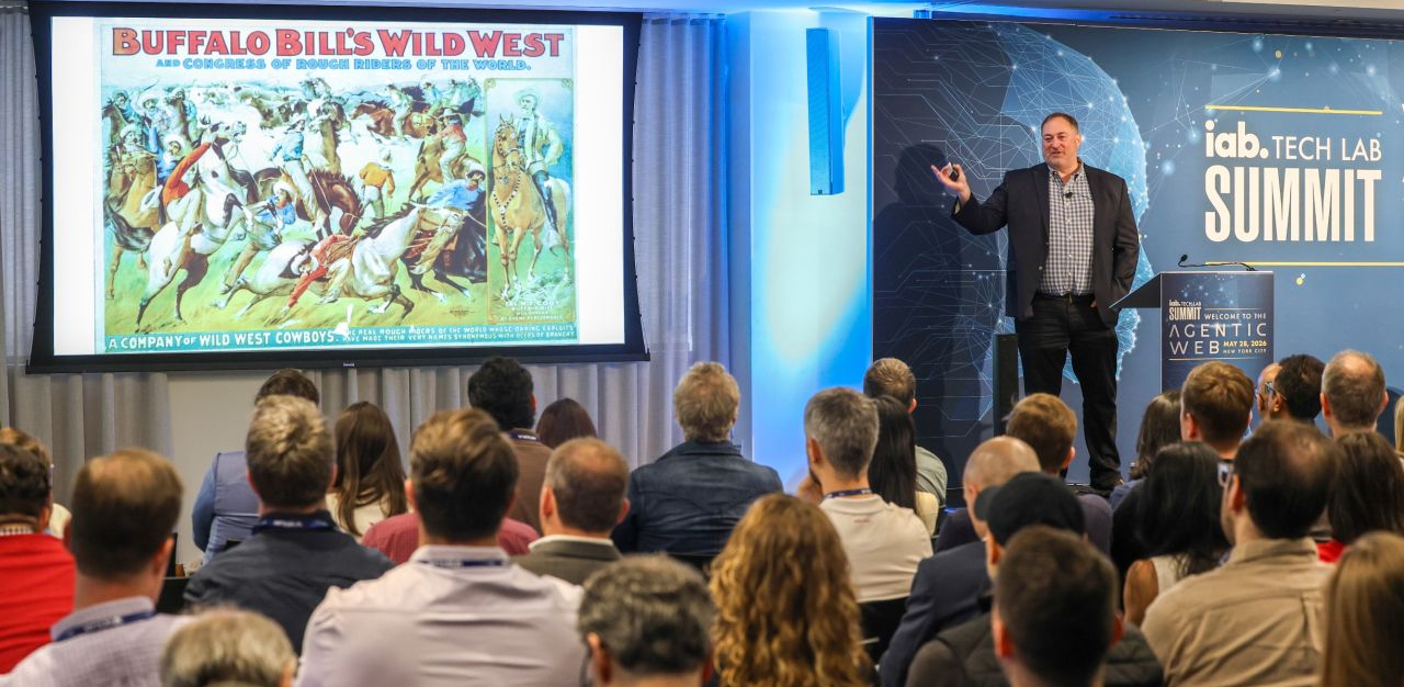A presenter from the IAB Tech Lab showing a vintage advertisement to a room full of marketing industry leaders.