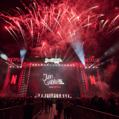 The massive stage for the Juan Gabriel Netflix screening in the Zócalo filled with fans. There are fireworks exploding in the background.